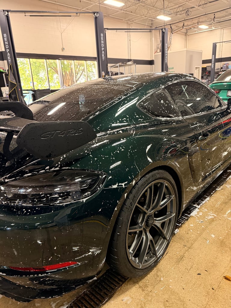 Dark green Porsche sports car in a garage bay with lift equipment and industrial ceiling