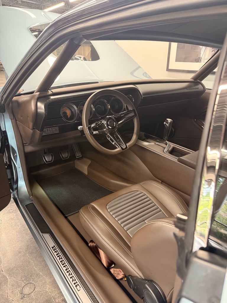 Interior of a classic car with tan leather seats, steering wheel, and dashboard visible through open drivers side door