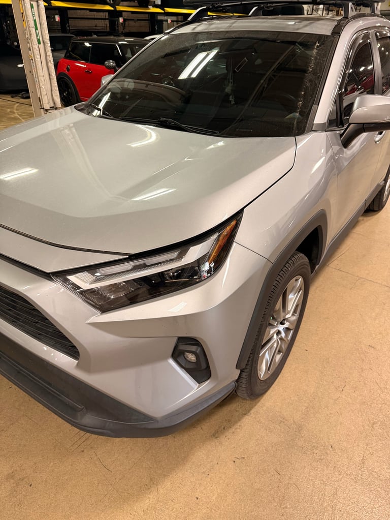 White Toyota RAV4 parked in a showroom with red and black vehicles visible in the background