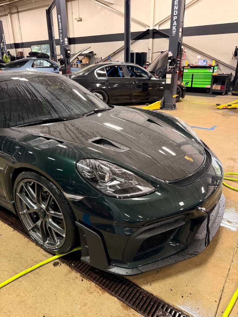 Dark green sports car in a garage with hydraulic lifts, undergoing maintenance or repair work
