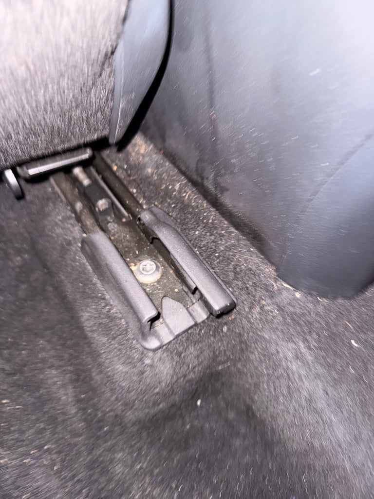 Close-up of a car seat base with gray fabric upholstery and metal attachment brackets visible underneath