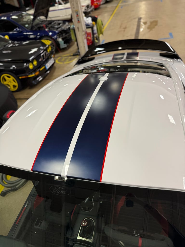 White sports car with blue and red racing stripes parked in garage with other custom vehicles