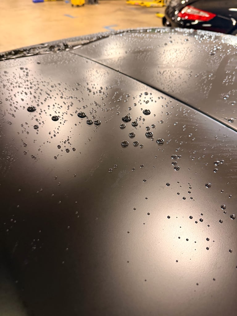 Close-up of wet metallic car hood with water droplets, workshop in background