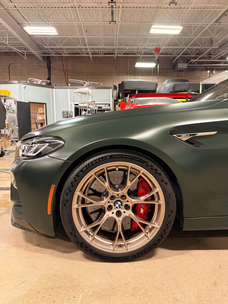 Close-up of a dark green sports car with bronze alloy wheels and red brake calipers in an industrial garage workshop