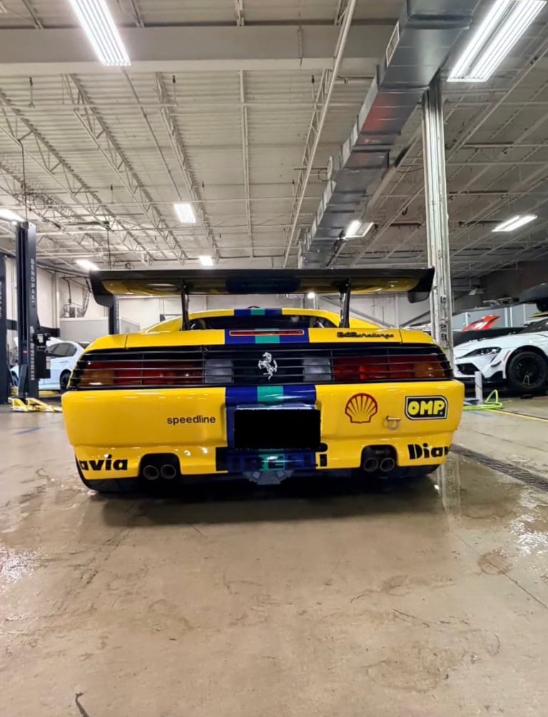 Yellow and red racing car with Ferrari branding on indoor warehouse floor with industrial ceiling lights