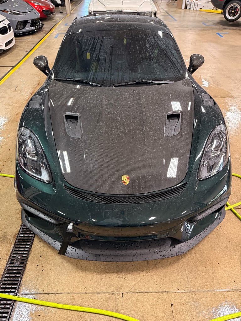 Dark green Porsche sports car on display in an indoor showroom with other vehicles visible in background