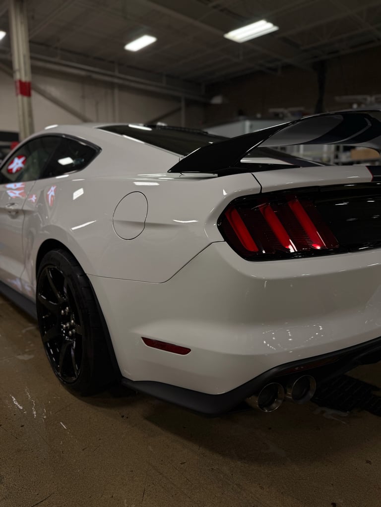 White Ford Mustang with hood open in indoor parking garage, showing rear view with illuminated taillights