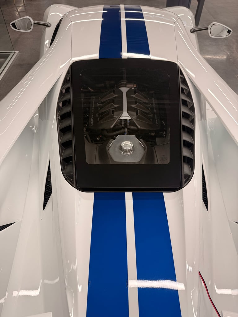 Overhead view of white sports car with blue racing stripes showing exposed engine through hood window