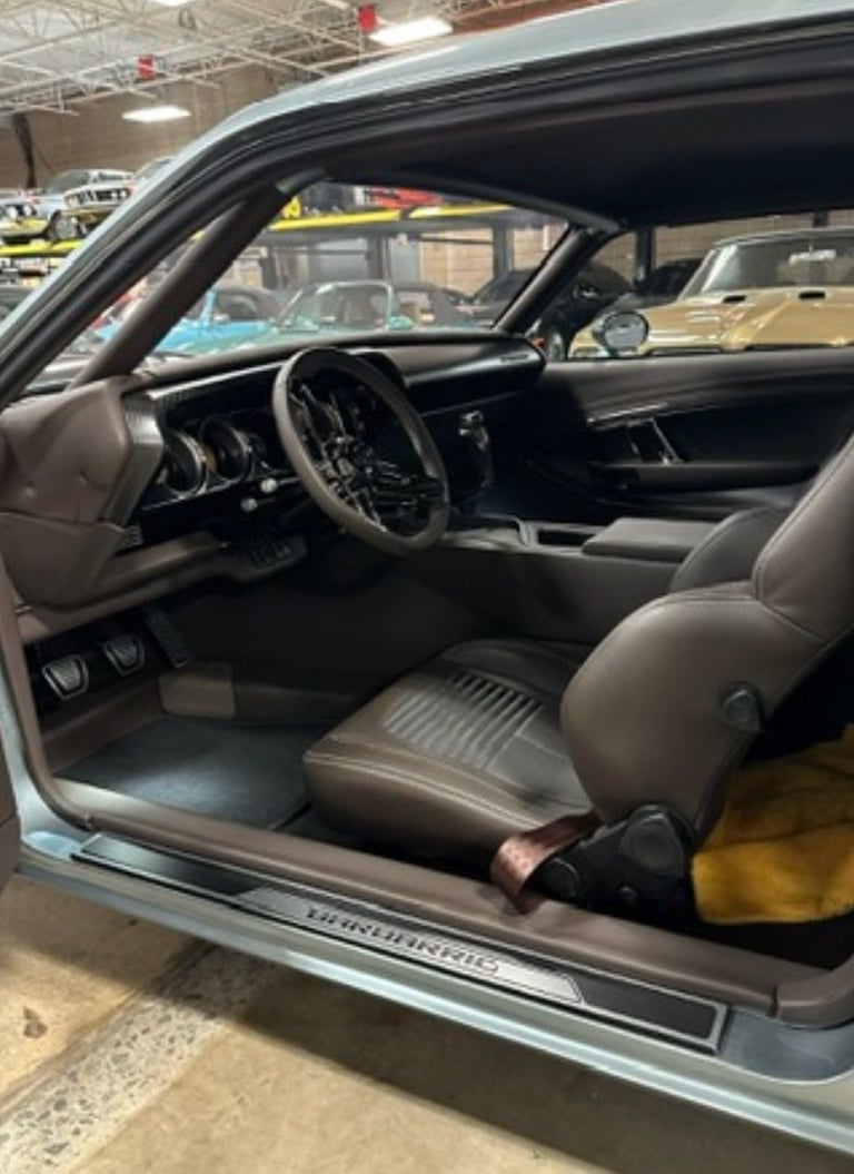 Interior of a classic car with black steering wheel, gray leather seats, and dashboard in a garage or showroom