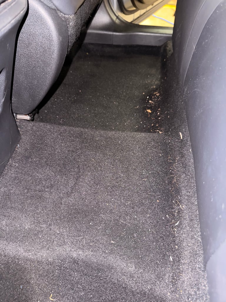 Dirty car interior floor with debris and dust visible near the seat area