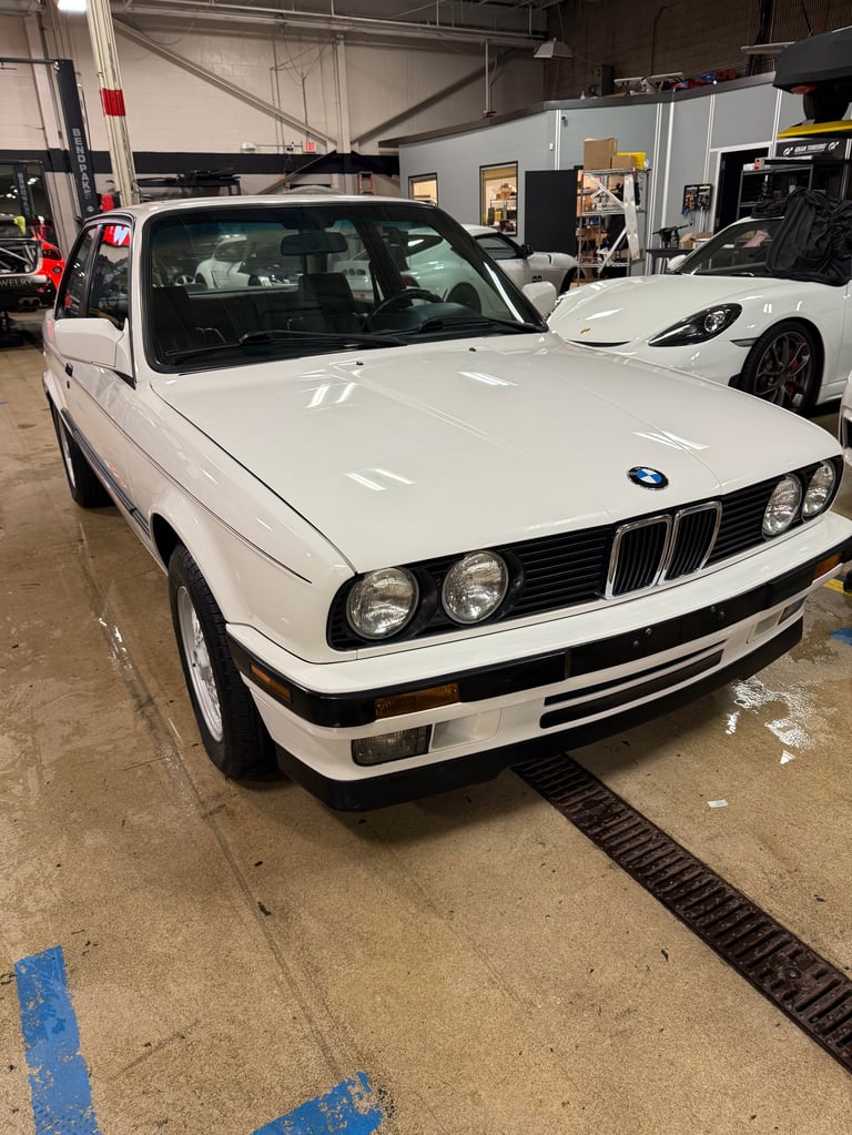 White BMW classic car parked in a showroom garage with other vehicles visible in the background