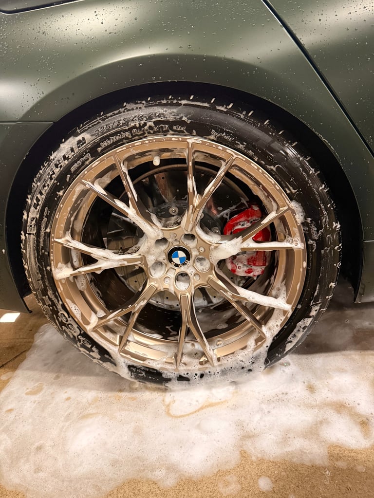 Close-up of a car wheel with muddy champagne-colored alloy rim and black tire, showing red brake caliper inside