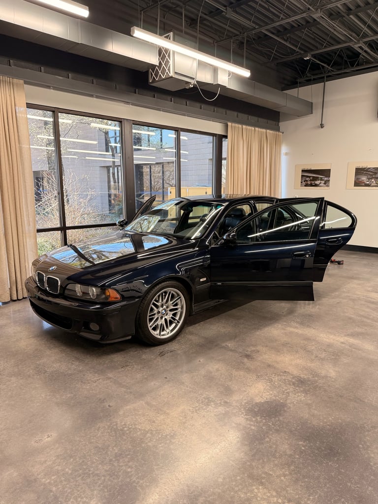 Black BMW sedan with driver door open displayed inside a modern warehouse showroom with large windows and industrial ceiling