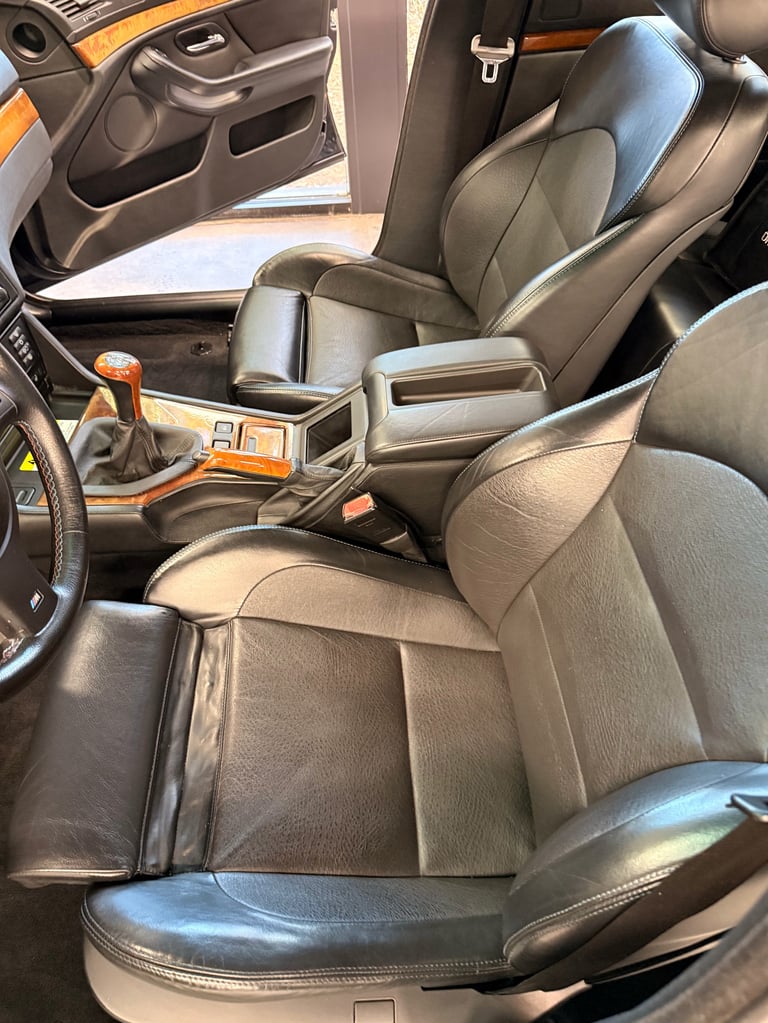 Interior view of a sports car showing black leather front seats with orange accents, steering wheel, and console with orange trim details